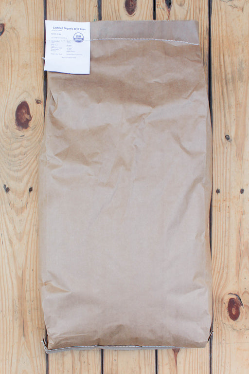 A brown kraft paper bag with a white product label at the top, laid flat on a light wood plank surface.