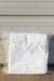 A folded white fabric item sealed in a clear plastic bag, with small printed text reading 'Agribon 19 83" x 50' on the bag, photographed against a light gray corrugated wall.