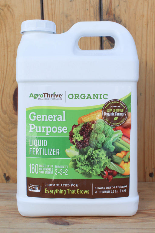 A white plastic jug of AgroThrive Organic General Purpose Liquid Fertilizer, featuring a green and brown label with an illustration of fresh vegetables, set against a rustic wooden background.