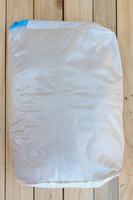 A large white woven sack or bag with a blue seal tape closure, photographed from above on a light-colored wooden plank surface.