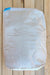 A large white woven sack or bag with a blue seal tape closure, photographed from above on a light-colored wooden plank surface.