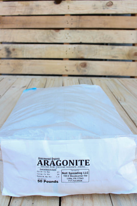 A 50-pound bag of Aragonite mineral supplement placed on a light-colored wooden plank surface, with a slatted wooden background.