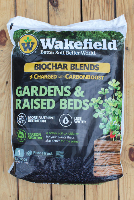 A bag of Wakefield Biochar Blends Gardens & Raised Beds soil amendment, placed on a wooden plank surface. The packaging is black with green, yellow, and white text and graphics, showing a potted plant.