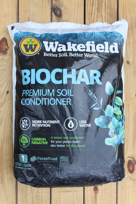A 1 cu ft bag of Wakefield Biochar Premium Soil Conditioner, displayed flat on a light-colored wooden plank surface. The packaging is primarily black with blue and white text, featuring the Wakefield brand logo and a graphic of green leaves.
