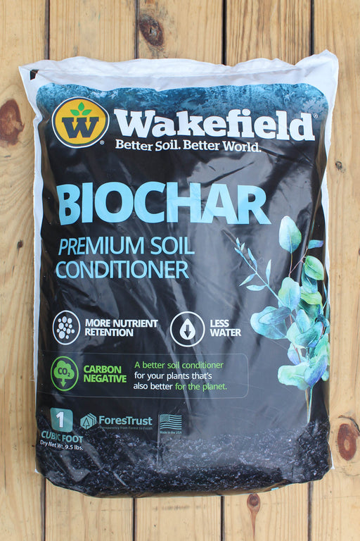 A 1 cu ft bag of Wakefield Biochar Premium Soil Conditioner, displayed flat on a light-colored wooden plank surface. The packaging is primarily black with blue and white text, featuring the Wakefield brand logo and a graphic of green leaves.