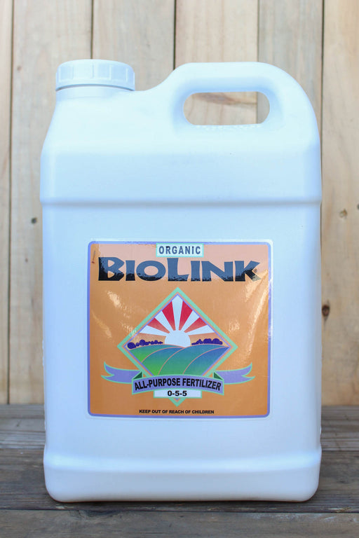 A large white plastic jug of Biolink Organic All-Purpose Fertilizer with a 0-5-5 label, set against a rustic wooden plank background.