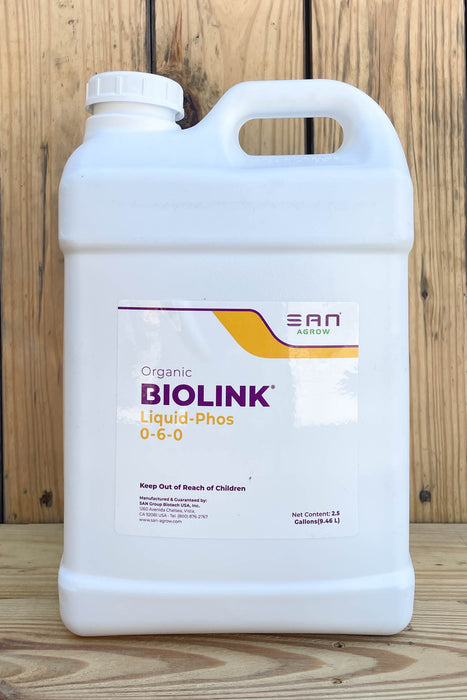 A large white plastic jug of BIOLINK Liquid-Phos 0-6-0 fertilizer, set against a rustic wooden plank background.