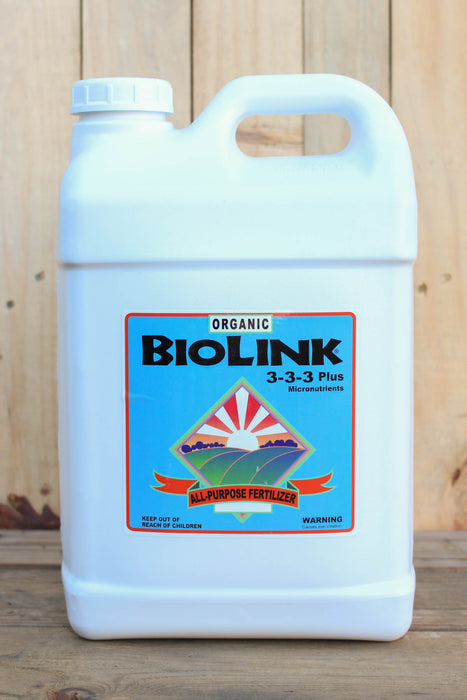 A white plastic jug of Biolink Organic 3-3-3 Plus All-Purpose Fertilizer with a blue and orange label, set against a rustic wooden background.