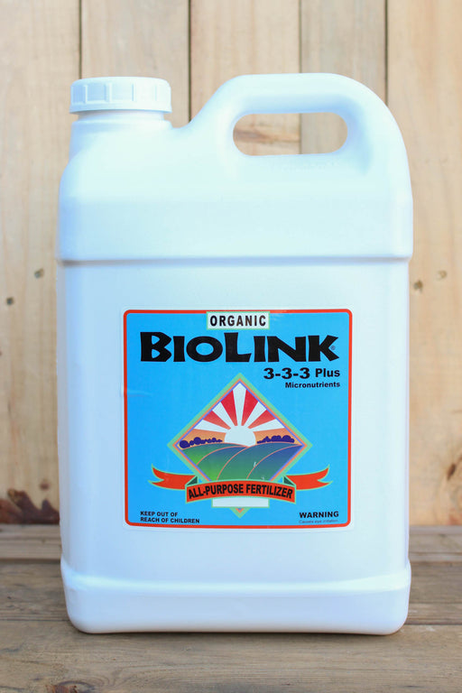 A white plastic jug of Biolink Organic 3-3-3 Plus All-Purpose Fertilizer with a blue and orange label, set against a rustic wooden background.