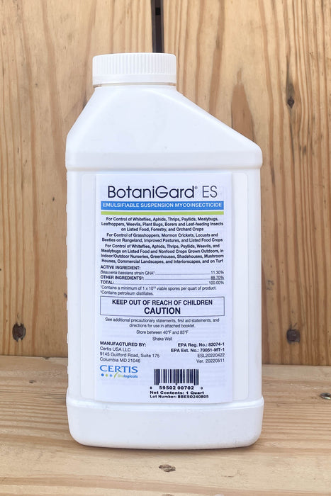 A white plastic bottle of BotaniGard ES, standing upright on a light-colored wooden surface against a wooden plank background.