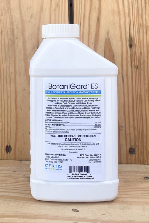A white plastic bottle of BotaniGard ES, standing upright on a light-colored wooden surface against a wooden plank background.