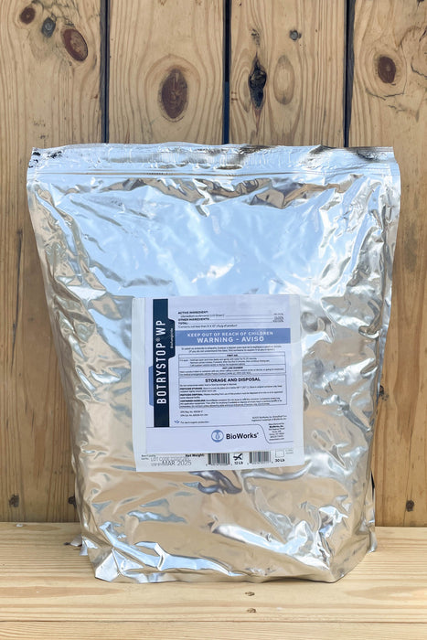 A large silver foil resealable bag of BotryStop WP standing upright against a rustic wooden plank background. A white product label is centered on the front of the bag.