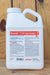 A white plastic jug of Brandt 719 Spreader with a detailed product label, photographed standing upright on a light-colored wooden surface.