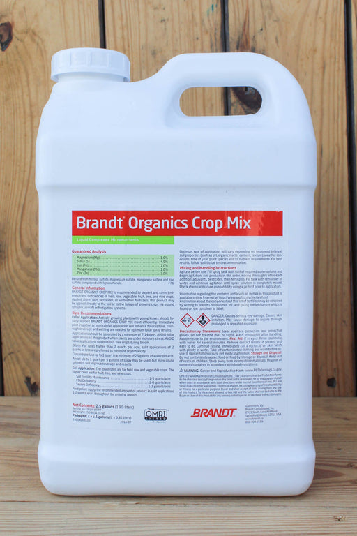 A large white plastic jug of Brandt Organics Crop Mix with a handle, standing on a wooden surface against a wooden plank background.
