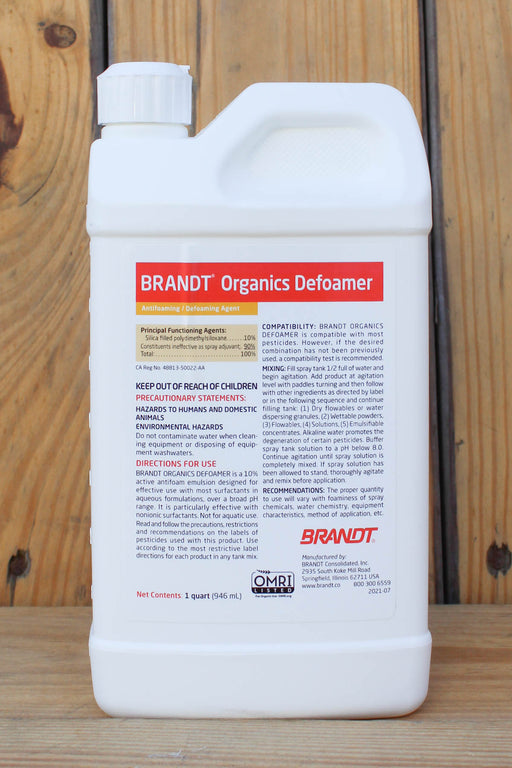 A white plastic bottle of BRANDT Organics Defoamer with a white cap, standing on a wooden surface against a wooden plank background. The label features red and black text and logos, including the prominent BRANDT logo.