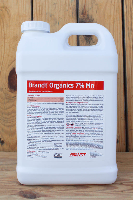 A large white plastic jug of Brandt Organics 7% Mn liquid fertilizer, featuring a white cap and a detailed red and black label, set against a rustic wooden plank background.