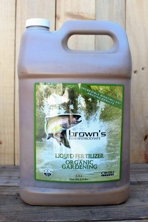 A large plastic jug of Brown's Liquid Fertilizer Organic Gardening, filled with a brownish liquid, set against a rustic wooden plank background.