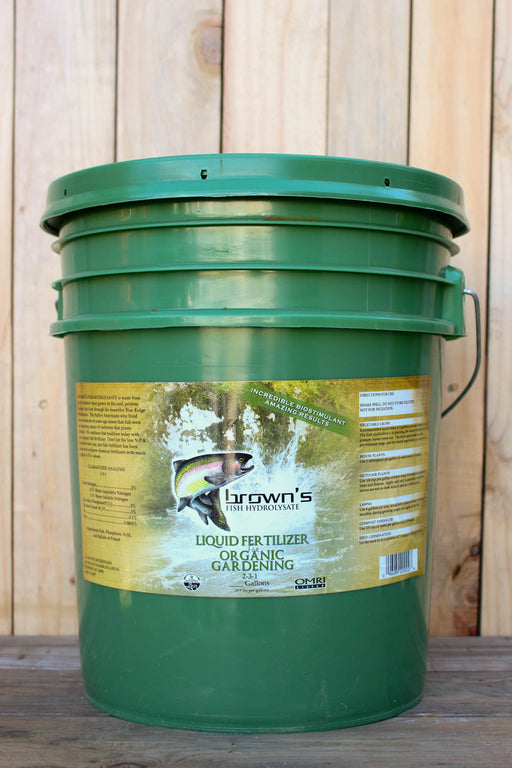 A green plastic bucket of Brown's Organic Liquid Fertilizer with a yellow label, set against a wooden plank background.