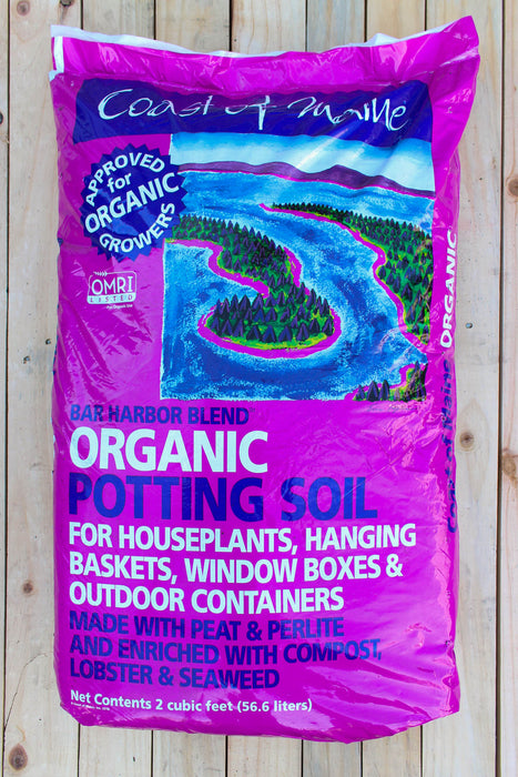A bag of Coast to Maine Organic Potting Soil, Bar Harbor Blend, displayed on a light-colored wooden plank background. The packaging is bright magenta pink with a central illustration of a winding blue river and green forest, and features an OMRI certification seal.