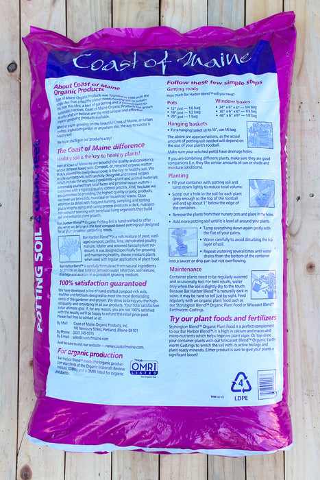 A large bag of OMRI Coast of Maine Potting Soil, featuring a white and purple label, photographed flat on a light-colored wooden plank background.