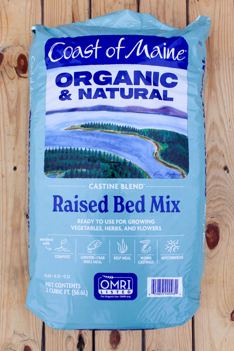 A 2 cubic foot bag of Coast of Maine Organic & Natural Raised Bed Mix, featuring a light blue bag with a scenic landscape illustration and product details, set against a light wood panel background.