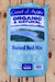 A 2 cubic foot bag of Coast of Maine Organic & Natural Raised Bed Mix, featuring a light blue bag with a scenic landscape illustration and product details, set against a light wood panel background.