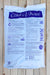A white bag of Coast of Maine Polished Stone Flour, displayed flat on a light-colored wooden plank surface. The packaging features a prominent blue header with the brand name 'Coast of Maine' in white script, and extensive blue text and instructional diagrams detailing the product's use and ingredients.