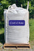 A large white bulk tote bag sitting on a wooden pallet outdoors, with green foliage and grass in the background. A purple label on the front reads 'Coast of Maine' in white script.
