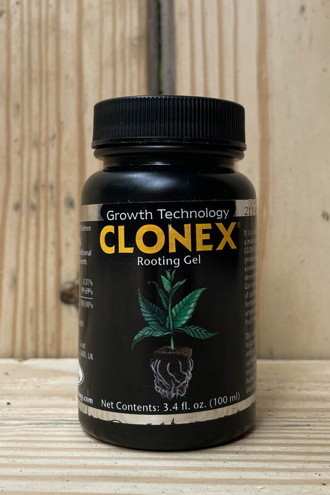 A black plastic bottle of CLONEX Rooting Gel with a black ribbed cap, set on a light wood surface against a light wood plank background. The label features the brand name 'CLONEX' in yellow, 'Growth Technology' in white, and an illustration of a green plant with a root system.