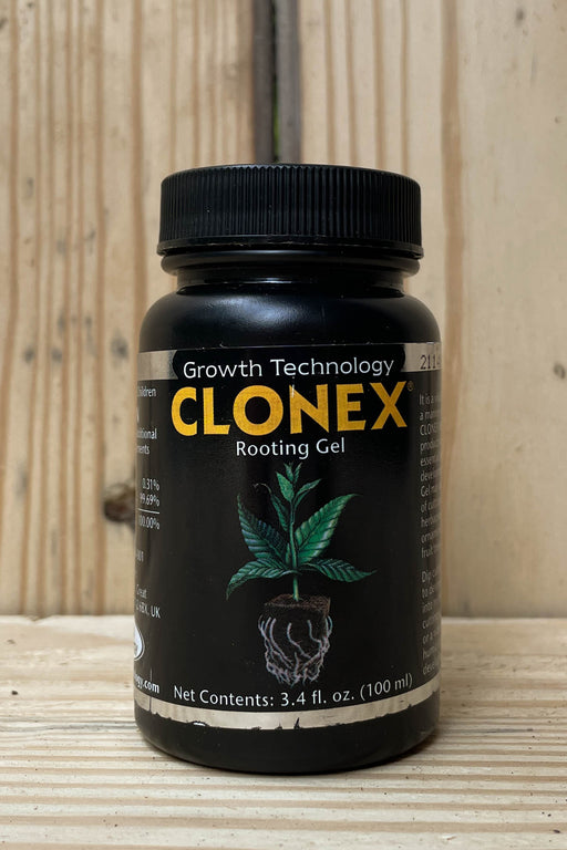 A black plastic bottle of CLONEX Rooting Gel with a black ribbed cap, set on a light wood surface against a light wood plank background. The label features the brand name 'CLONEX' in yellow, 'Growth Technology' in white, and an illustration of a green plant with a root system.
