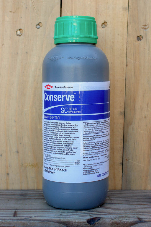 A bottle of Conserve SC turf and ornamental insect control, featuring a green cap and a blue and white label, set against a wooden plank background.