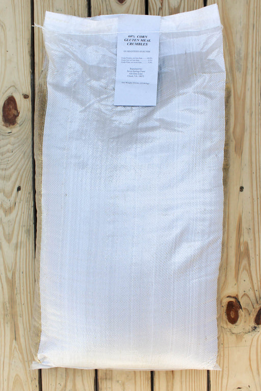 A large white woven sack of corn gluten meal lies flat on a light wood plank surface, with a small white label attached near the top.