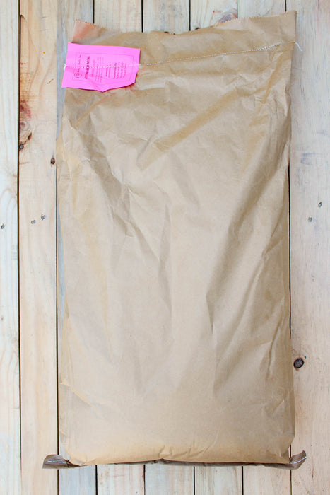A large brown paper bag with a bright pink  label, laid flat on a light-colored wooden plank surface.
