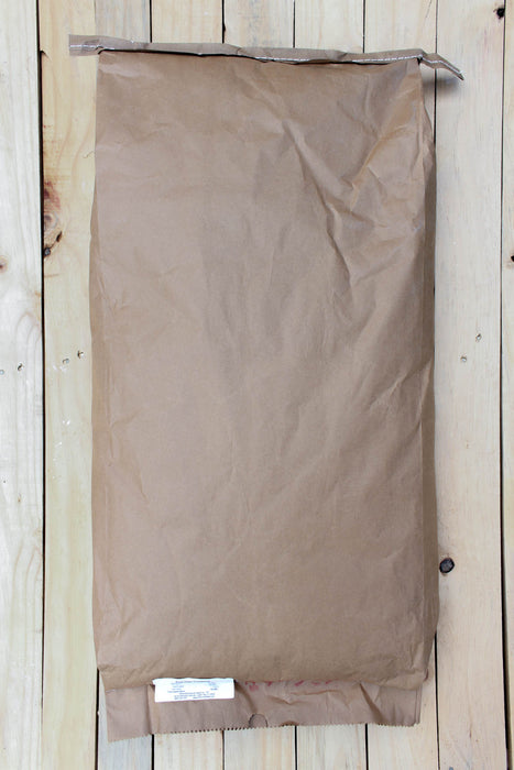 A brown paper bag with a crimped top edge and a small white label at the bottom, laid flat on a light wood plank background.