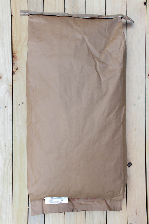 A brown paper bag with a crimped top edge and a small white label at the bottom, laid flat on a light wood plank background.
