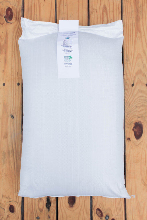 A white bag of crimson clover laid flat on a wooden plank surface, with a white product tag attached at the top.