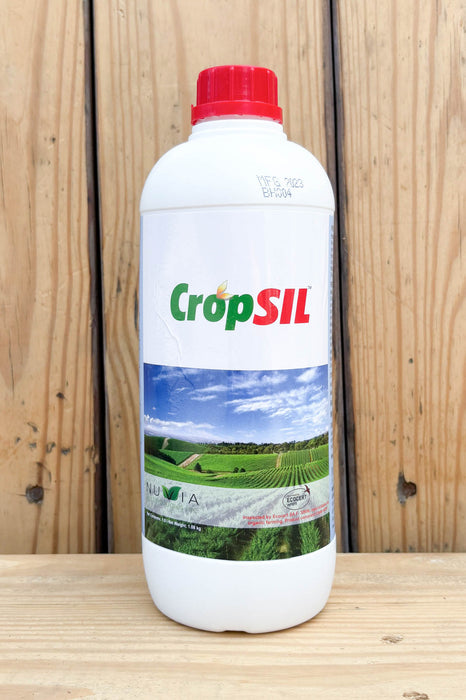 A white plastic bottle of CropSIL with a red cap, standing on a wooden surface against a wooden plank background.