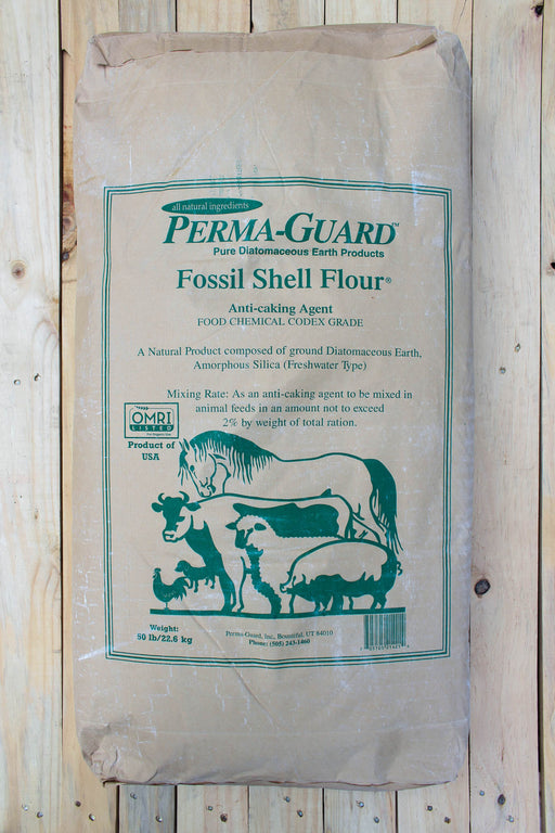 A large paper bag of Perma-Guard Fossil Shell Flour anti-caking agent, featuring green text and illustrations of farm animals on a beige background, photographed against a light wood plank wall.