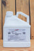 A white plastic jug of Debug Bug Turbo liquid pesticide with a handle and a detailed white label, set against a rustic wooden plank background.
