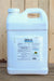 A large white plastic jug of DES-X with a handle and a white cap, standing on a wooden surface against a wooden plank background.