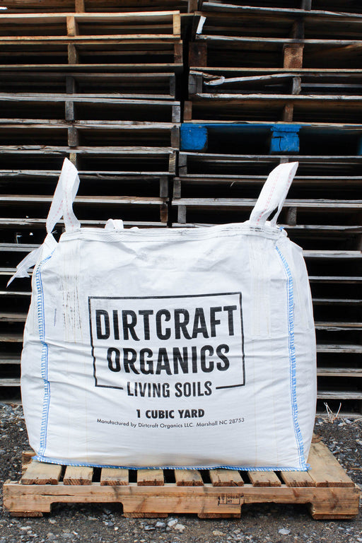 A large white bulk bag of Dirtcraft Organics Living Soils, 1 cubic yard, displayed on a wooden pallet in front of a stack of wooden pallets.
