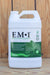 A white plastic bottle of EM-1 Effective Microorganisms concentrated microbial inoculant, featuring a green and white label, set against a rustic wooden plank background.
