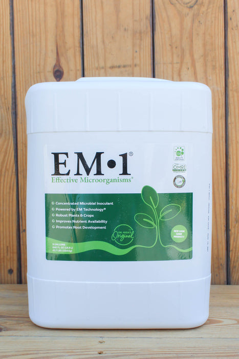 A white plastic bucket of EM-1 Effective Microorganisms concentrated microbial inoculant, featuring a green and white label, set against a rustic wooden plank background.
