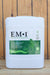 A white plastic bucket of EM-1 Effective Microorganisms concentrated microbial inoculant, featuring a green and white label, set against a rustic wooden plank background.