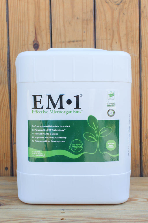 A white plastic bucket of EM-1 Effective Microorganisms concentrated microbial inoculant, featuring a green and white label, set against a rustic wooden plank background.