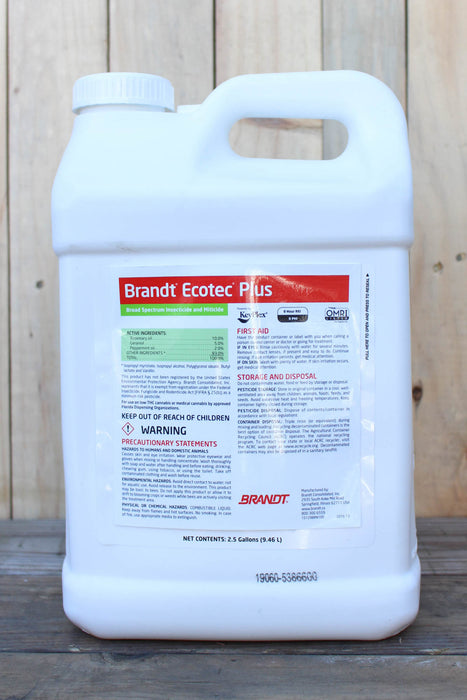 A 2.5 gallon white plastic jug of Brandt Ecotec Plus, standing on a dark wooden surface against a light wood plank background.