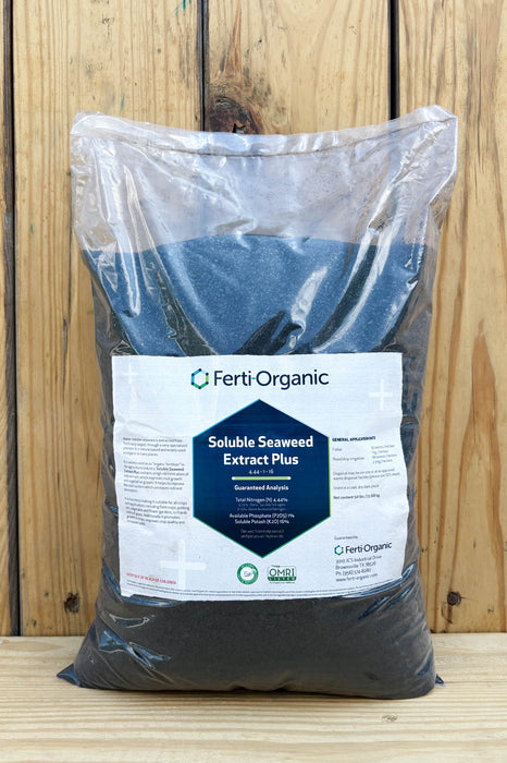 A large clear plastic bag filled with dark charcoal-colored Ferti Organic Soluble Seaweed Extract Plus, featuring a white and blue label, set against a rustic wooden plank background.