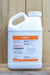 A white plastic jug of Fulmax, featuring an orange and white label, set against a rustic wooden plank background.