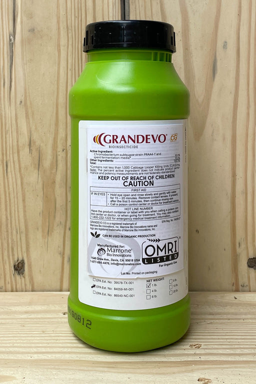 A green plastic bottle of Grandevo with a black cap, standing on a light wood surface against a wood panel background.