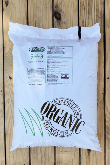 A large white bag of BioSystems Nitrogen 5-4-3 slow-release fertilizer with calcium, displayed on a light-colored wooden plank background.